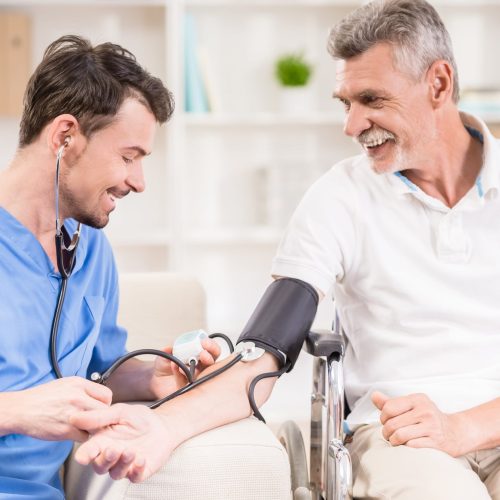 Healthcare worker checking an older patient's blood pressure during a home nursing visit in Islamabad