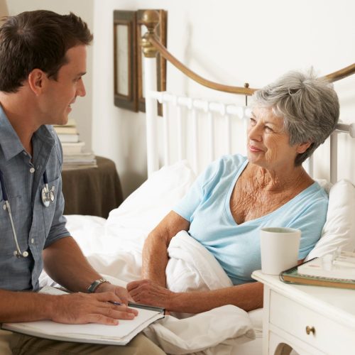Doctor talking with a senior patient in bed during a home visit in Islamabad